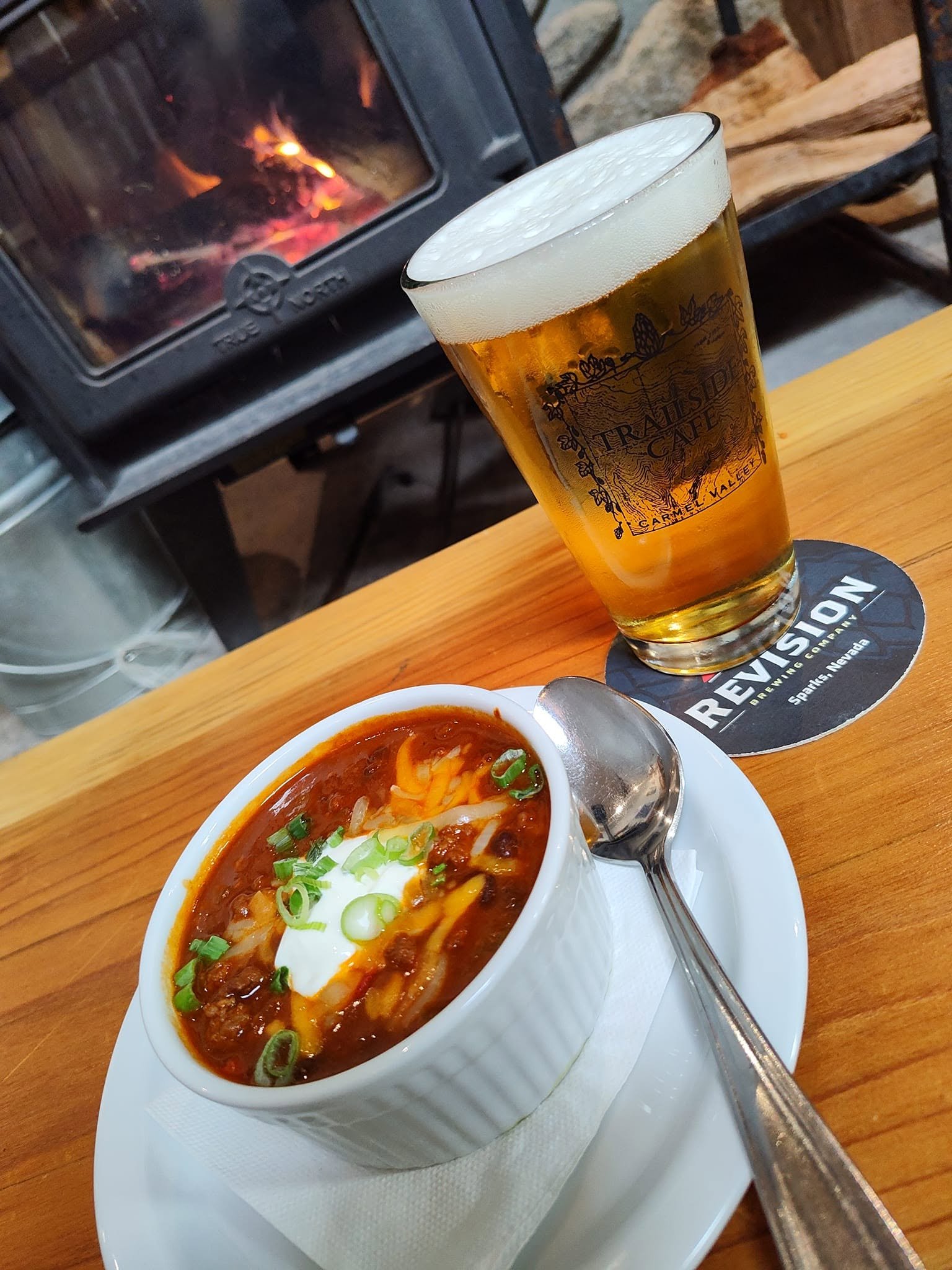 A bowl of chili and a branded Trailside pint beside the wood-burning stove