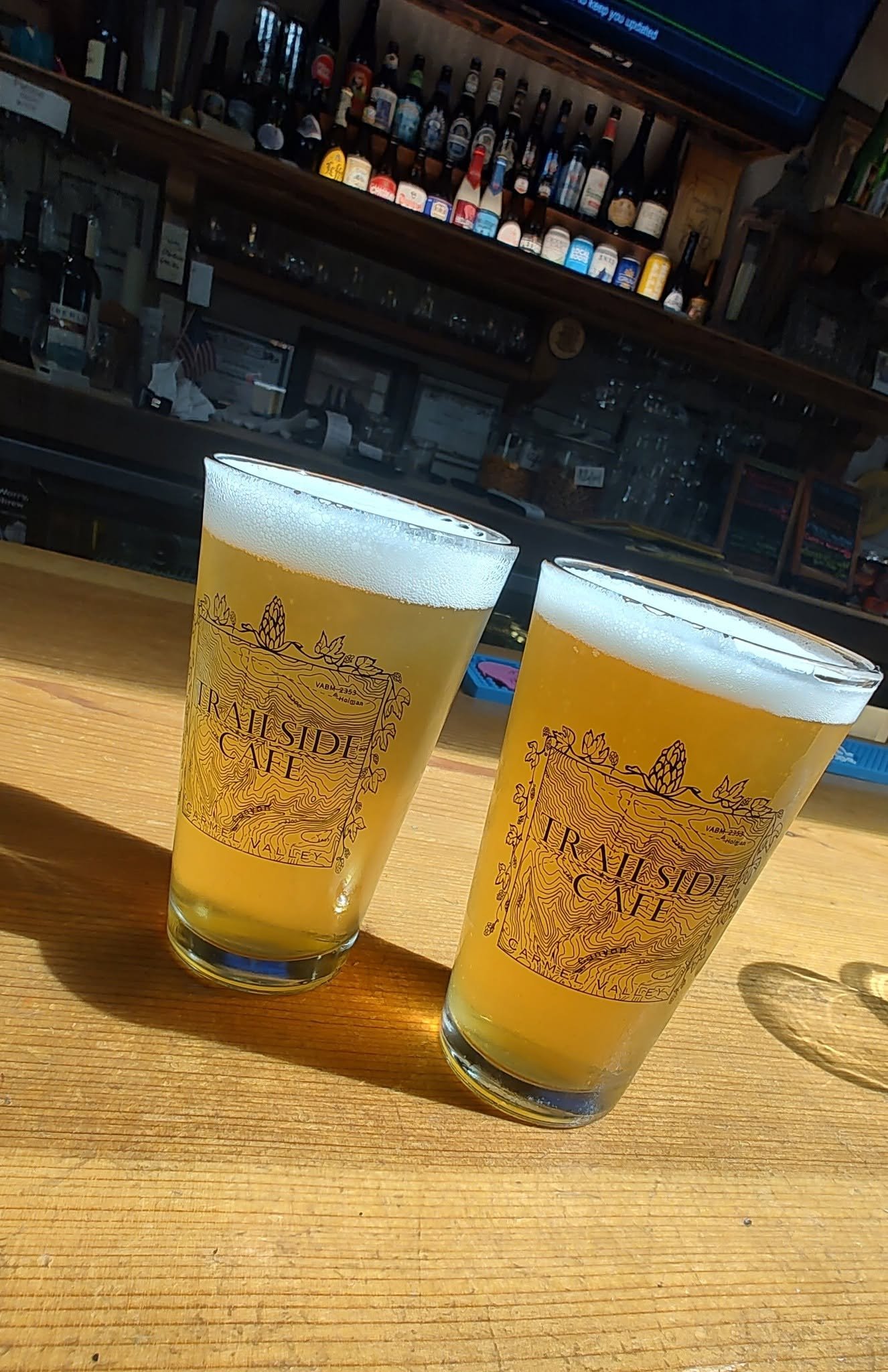 Two Trailside pint glasses with the topographic logo on the bar